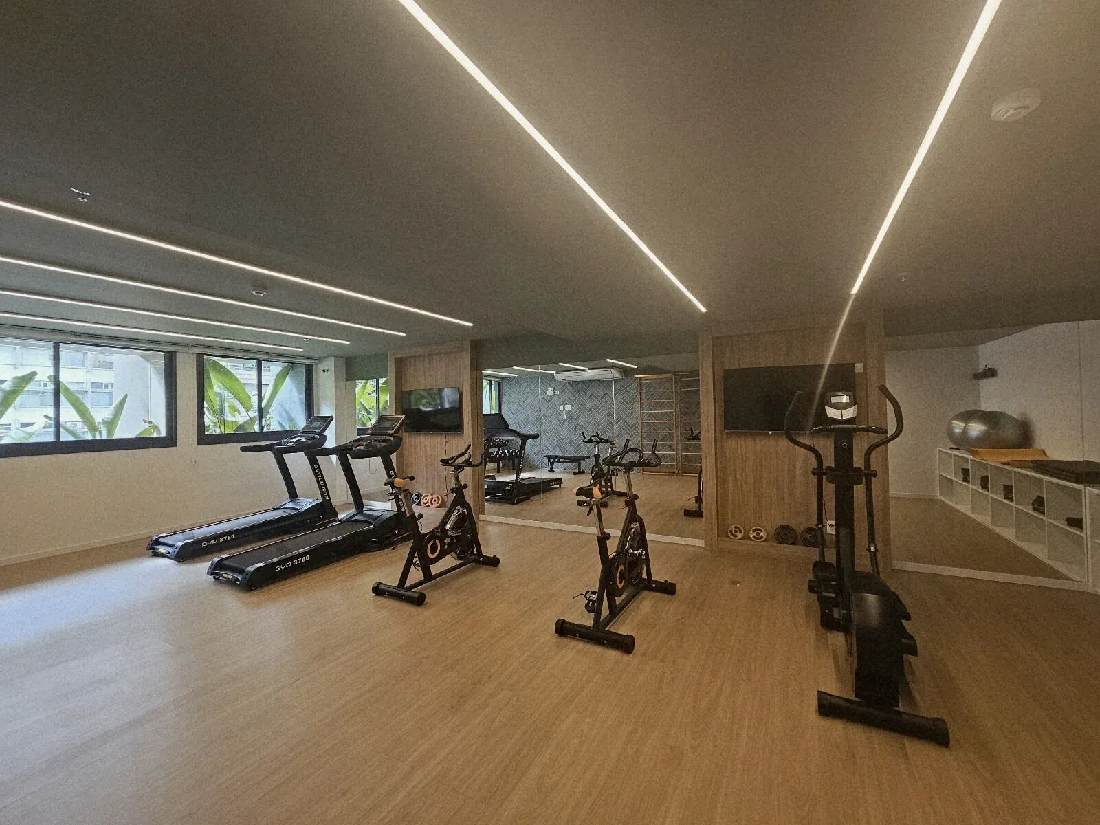 Sala de estar decorada integrada à varanda de um apartamento tipo no Alma Ipanema, com piso de alto padrão e painéis de madeira.